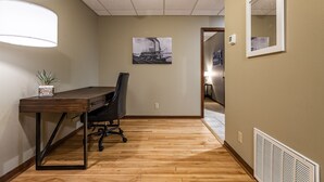 Une pièce avec un plancher en bois, un bureau avec une chaise, une lampe fixée au mur, un tableau encadré et un radiateur.
