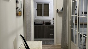 Um corredor estreito com uma cozinha compacta, uma porta de vidro deslizante e um quadro na parede.