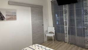 Quarto com cama, cadeira, televisão, porta e cortinas.