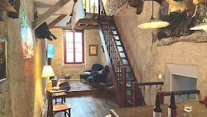 Een rustiek interieur met een houten trap, een eethoek met een tafel en stoelen, en een bar met flessen.