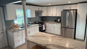 A modern kitchen with white cabinets, stainless steel appliances, and a marble countertop. - Beach house - 3 min walk to beach! (Englewood)