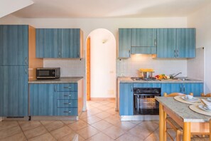 A modern kitchen with blue cabinets, a microwave, stove, oven, and a dining area with a table and chairs. - Le Dimore di Budoni Trilocale, Budoni, Italy (Budoni)