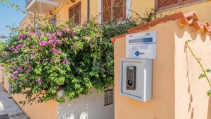 A key box with a keypad, a sign indicating 'Residence Le Pavencelle,' and a building with balconies and shutters.