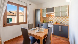 Una cuina petita amb taula de menjador, cadira i finestra amb cortines.