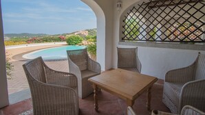 A covered patio with wicker furniture, a pool, and a view of the landscape. - Il Giardino Degli Oleandri Bilo 4, Porto Cervo, Italy (Porto Cervo)