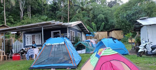 A campsite with multiple tents, a small building with a corrugated metal roof, and a white scooter parked nearby.