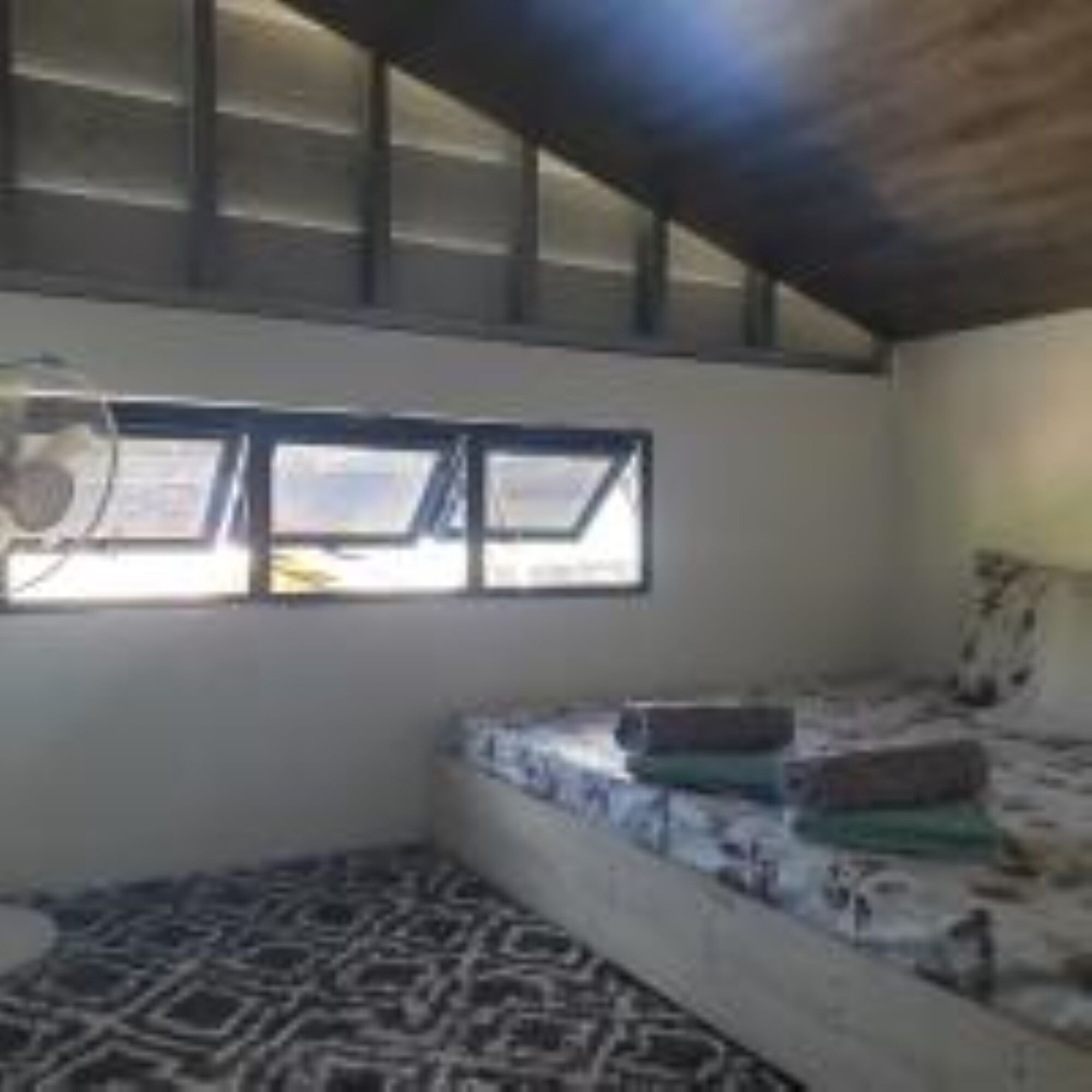 A small, single-room cabin with a sloped ceiling, a window, and a bed with patterned bedding.