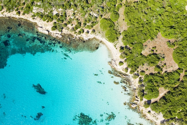 An aerial view of a coastal area with clear turquoise waters, sandy beaches, and dense green vegetation.