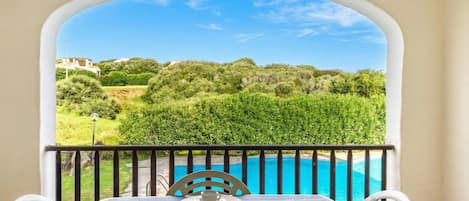 A balcony with a table set for four, overlooking a swimming pool and lush greenery.