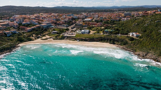 Un pueblo costero con playa, edificios y montañas al fondo.