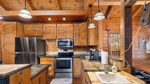 Une cuisine de style rustique, avec des éléments en bois, comprenant un réfrigérateur, un four à micro-ondes, une cuisinière et un évier.