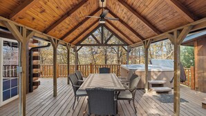 Une terrasse extérieure couverte avec un plafond en bois, une table avec des chaises et un jacuzzi.