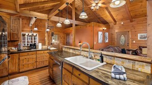 L’intérieur d’un chalet rustique, avec un revêtement mural en bois, une grande cuisine dotée d’un plan de travail en pierre et un coin salon confortable.