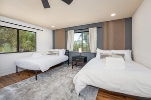 Un dormitori modern amb dos llits individuals, una petita taula de nit amb una làmpada, i una finestra gran amb cortines.