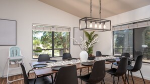 A dining area with a long table, black chairs, a white vase with flowers, and a hanging light fixture. - Yosemite zen, Pool, Hot tub, Private suite and Views! (oakhurst)