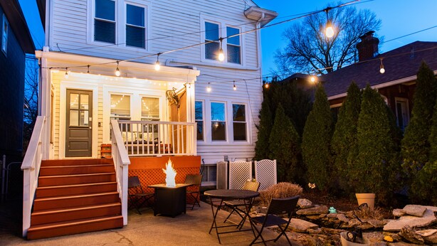 A white house with a porch, outdoor seating, and a fire pit.