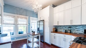A modern kitchen with white cabinets, a stainless steel refrigerator, a wooden countertop, and a chandelier.