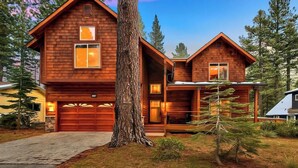 A two-story log cabin with a garage, surrounded by trees.