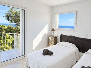 Un dormitorio con cama, cómoda, lámpara y vista al mar desde un balcón.