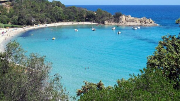 A coastal beach with clear turquoise waters, boats, and a sandy shore.