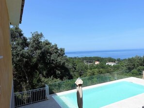 On peut admirer une piscine dont l’eau est d’une clarté parfaite, séparée du reste par une barrière de verre, et qui est entourée d’une végétation luxuriante. On aperçoit également la mer au loin.