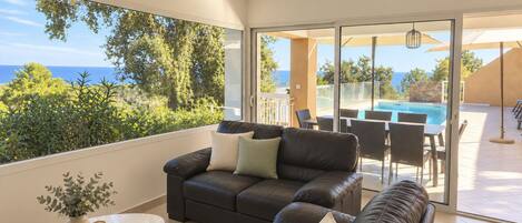A modern living room with a leather sofa, a small table, and a view of a pool and ocean.