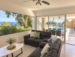 Un salon moderne avec un canapé en cuir, une petite table et une vue sur une piscine et l’océan.