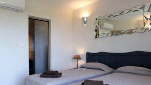 A hotel room with two beds, a mirror, a lamp, and an air conditioning unit.