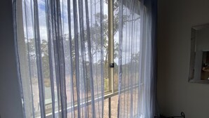 Una habitación con un gran ventanal cubierto por cortinas traslúcidas, una pequeña mesa y una silla.
