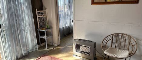 Ein Zimmer mit großem Fenster, Heizkörper, Korbsessel und einem gemusterten Teppich.