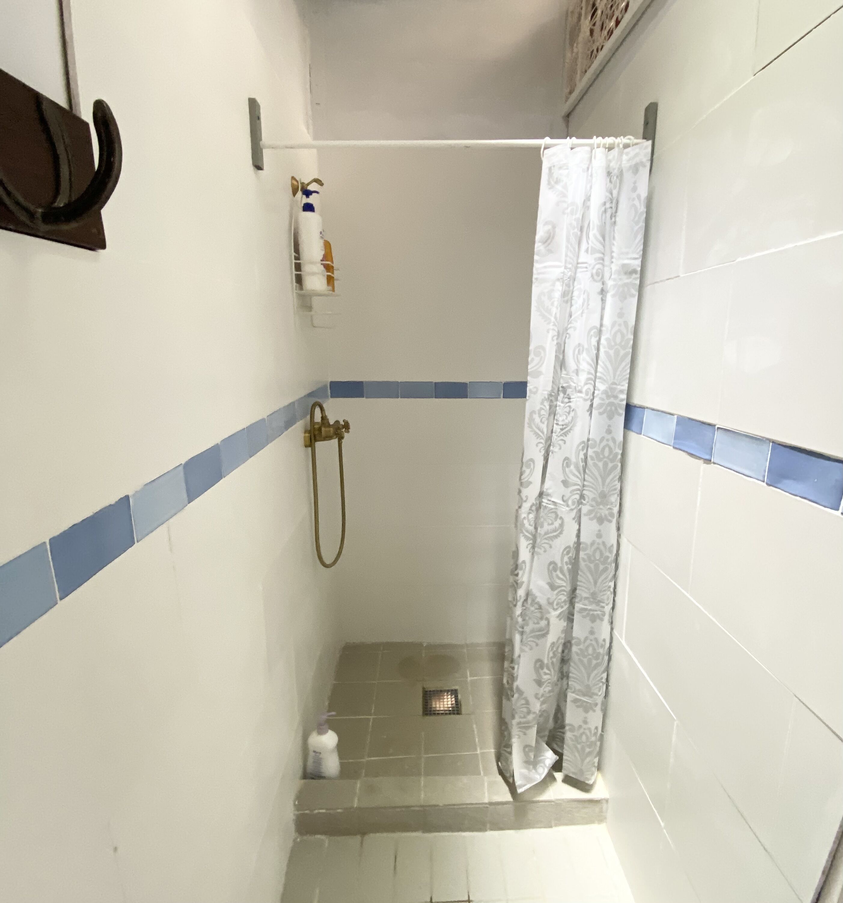 A small, tiled shower area with a shower curtain, a towel rack, and a bottle of shampoo.
