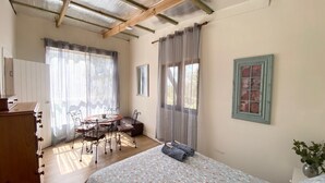 Un dormitorio con una cama, un aparador de madera, una mesita con sillas y una ventana con cortinas.