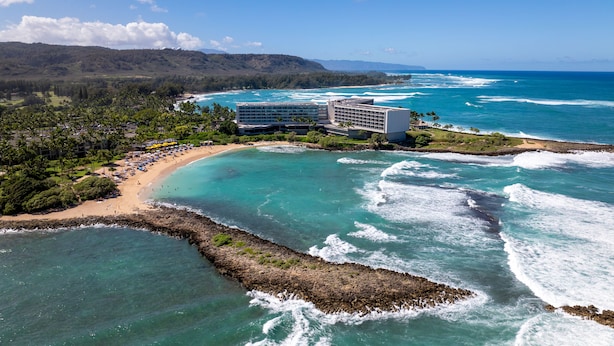 A coastal hotel with a beach, ocean views, and a mountainous backdrop. - Hale Kuilima: Condo on the Golf Course at Turtle Bay (Kahuku)