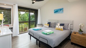 A modern bedroom with a large bed, a ceiling fan, a view of greenery through the window, and a small bedside table with a plant. - Hale Kuilima: Condo on the Golf Course at Turtle Bay (Kahuku)