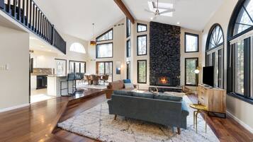 A spacious living area with a fireplace, large windows, and a staircase.