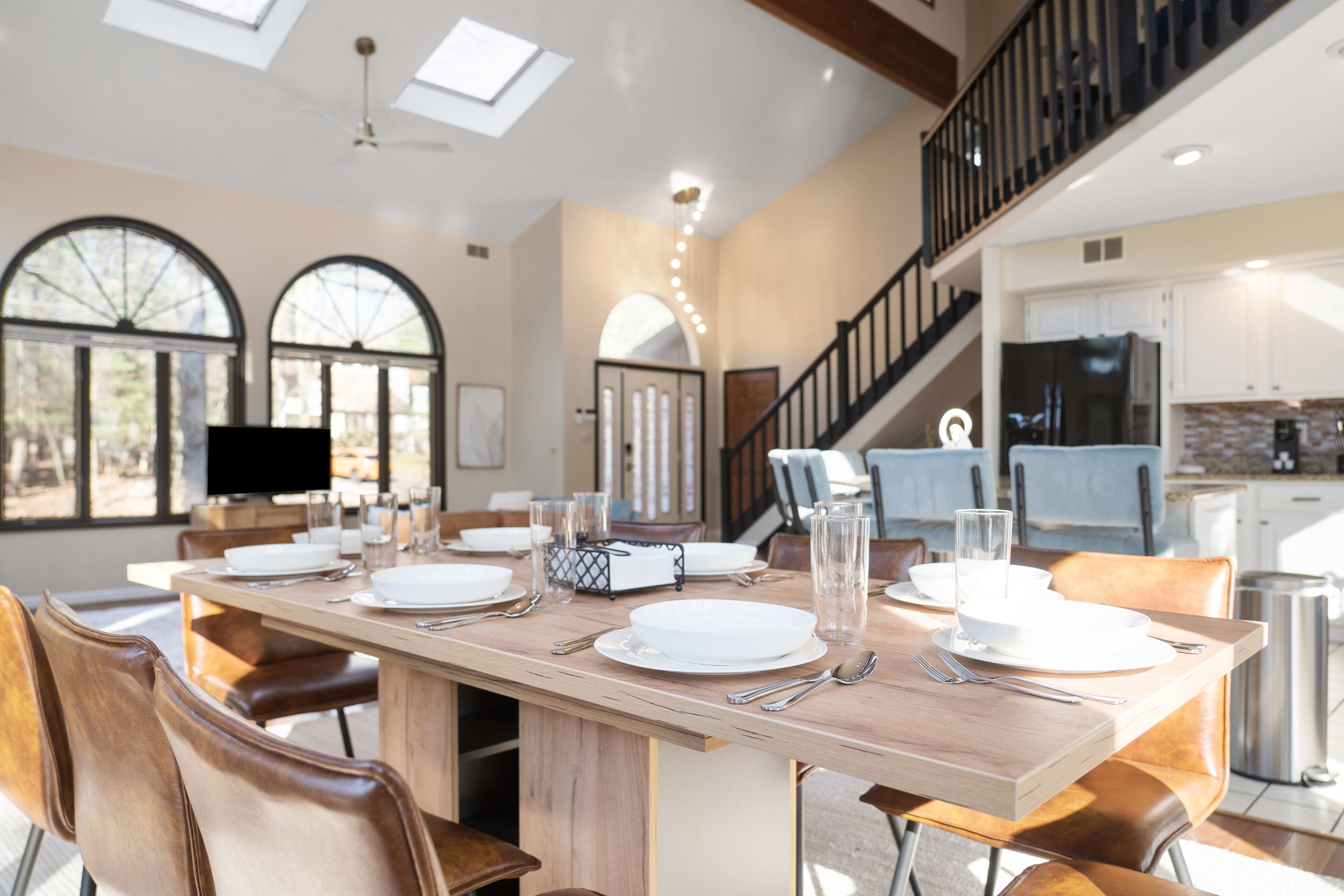 A dining area with a long table set for six, wooden chairs, and a kitchen in the background.