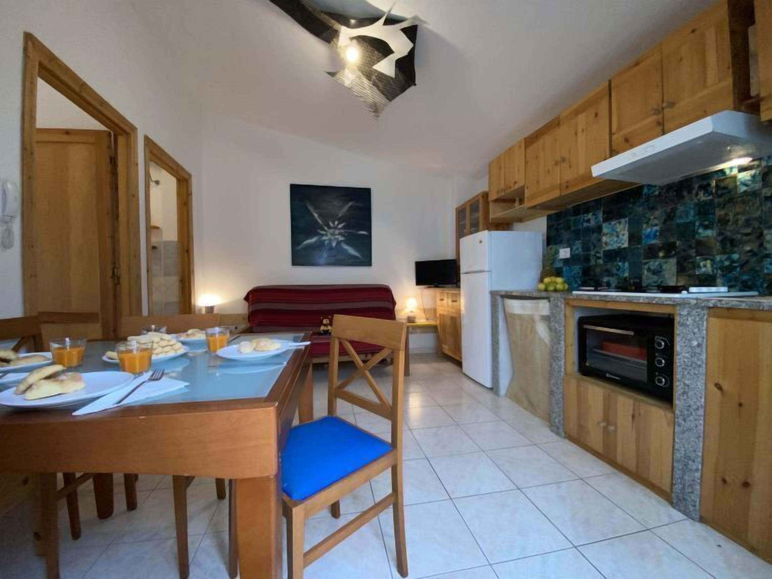 Une cuisine avec des meubles de rangement en bois, une table à manger avec des chaises, un canapé rouge et un téléviseur.