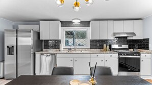 Una cucina moderna con elettrodomestici in acciaio inossidabile, un pannello decorativo in piastrelle nere e un'area pranzo con un tavolo scuro.