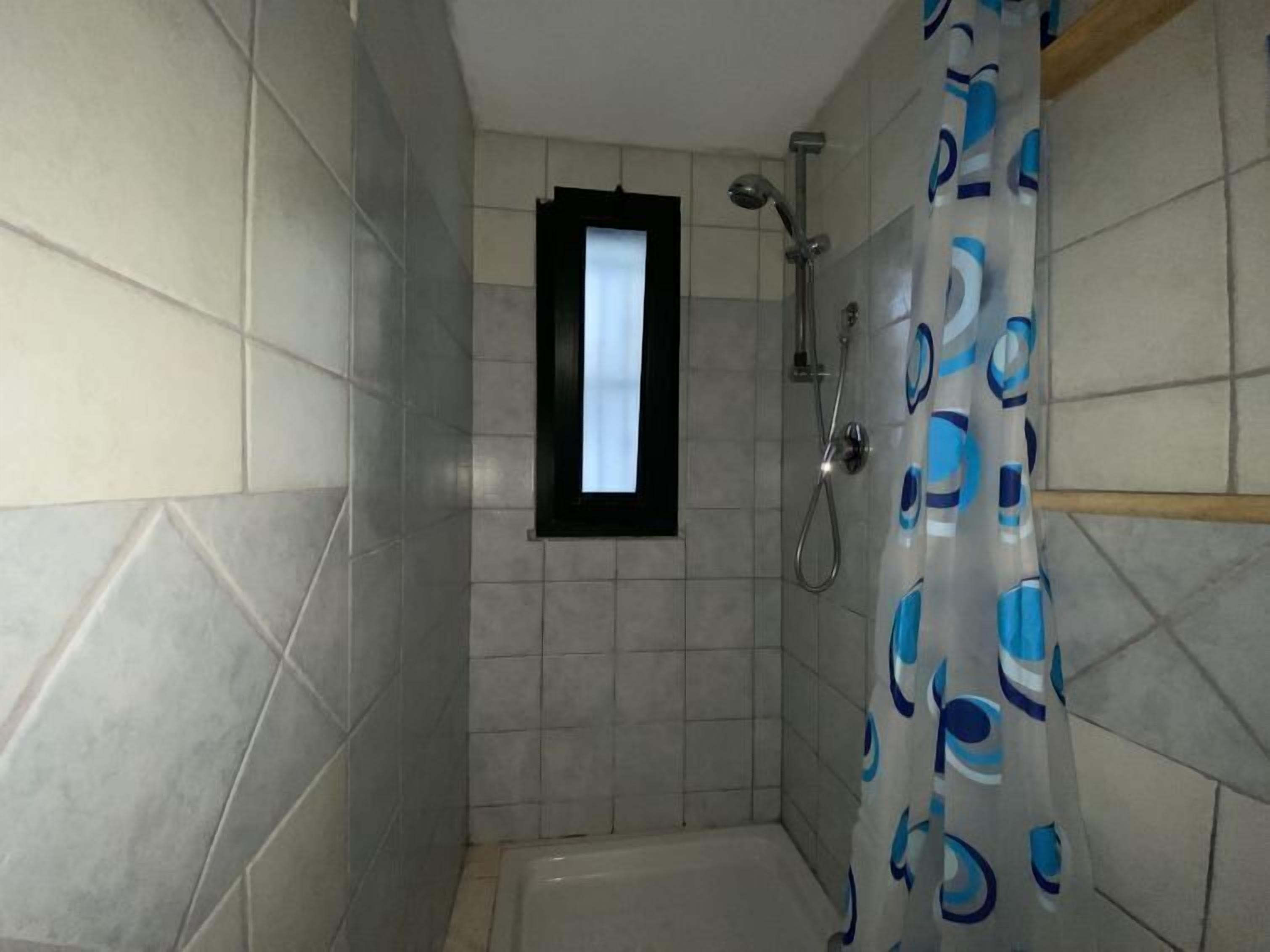 A small, tiled shower room with a window and a shower curtain.
