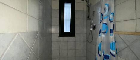 A small, tiled shower room with a window and a shower curtain.