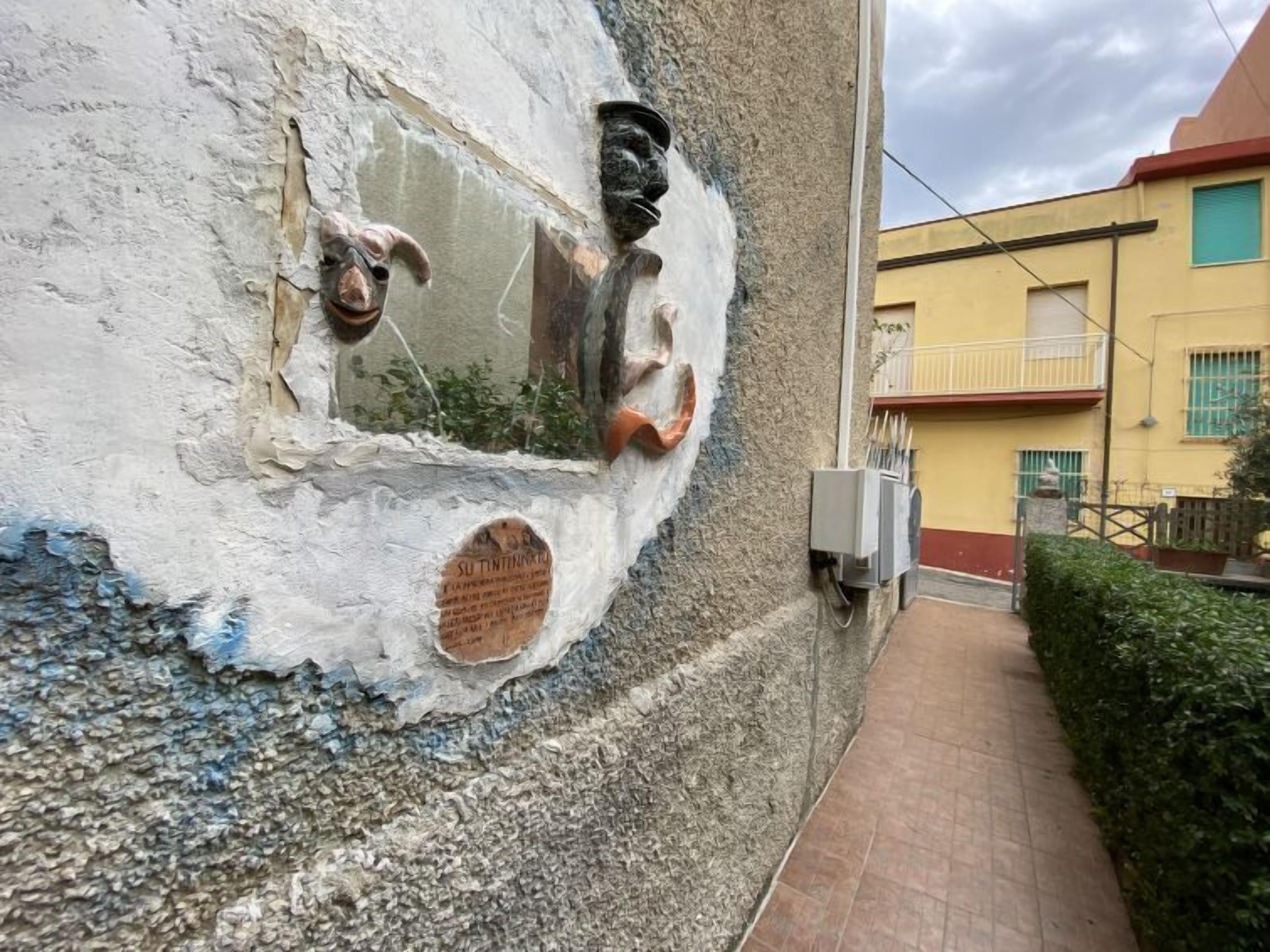 Eine strukturierte Wand mit einer Metallskulptur und einer Tafel.