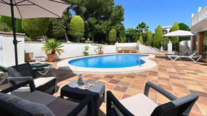 A pool area with wicker furniture, a round table, and a small garden with potted plants. - Puravida - Javea, Costa Blanca (Javea)