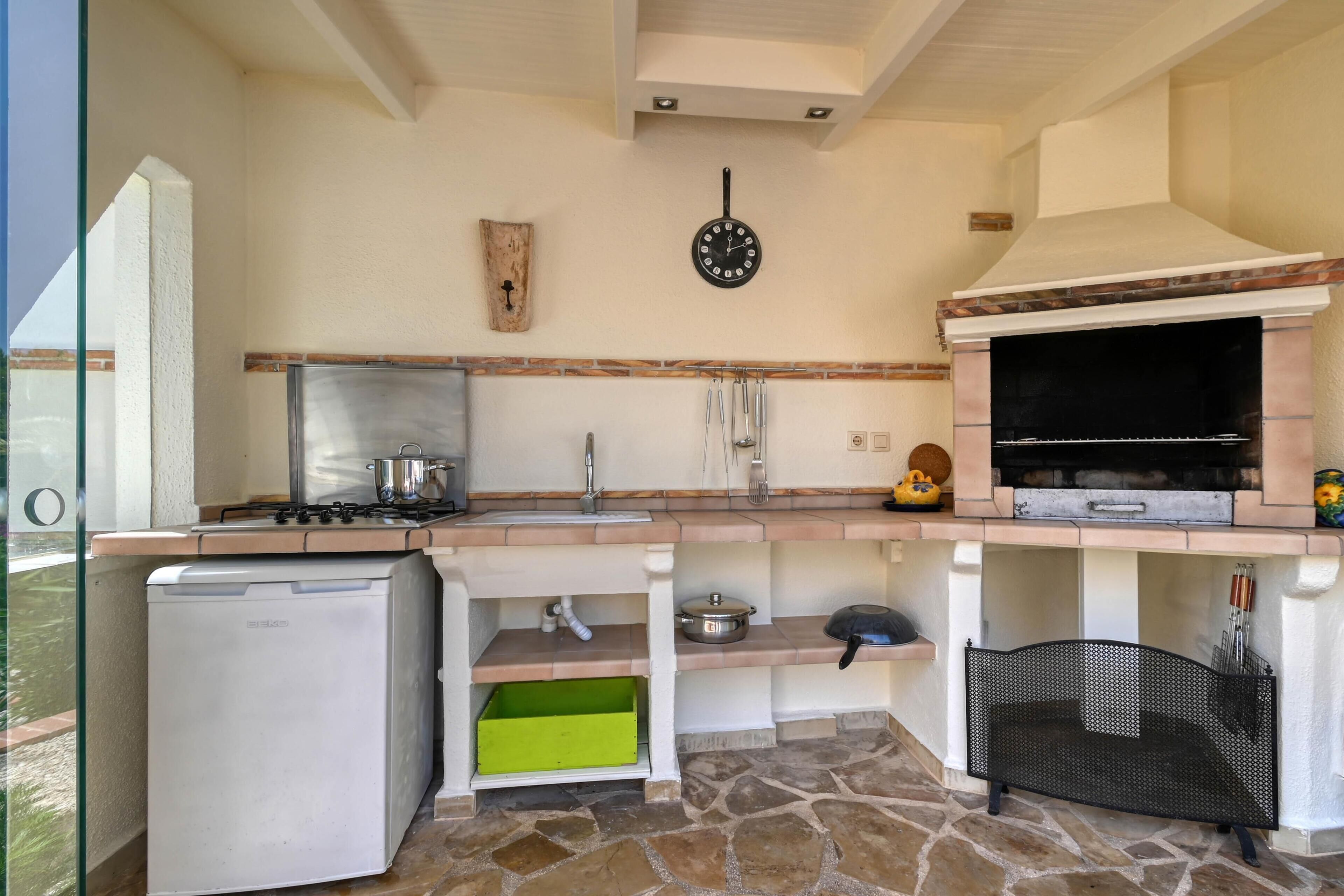 A kitchen with a built-in grill, a refrigerator, and a sink.