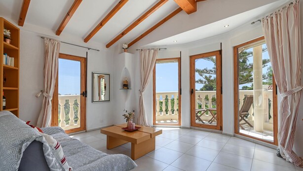 A spacious living room with a sofa, a wooden coffee table, and large windows with curtains. - Puravida - Javea, Costa Blanca (Javea)