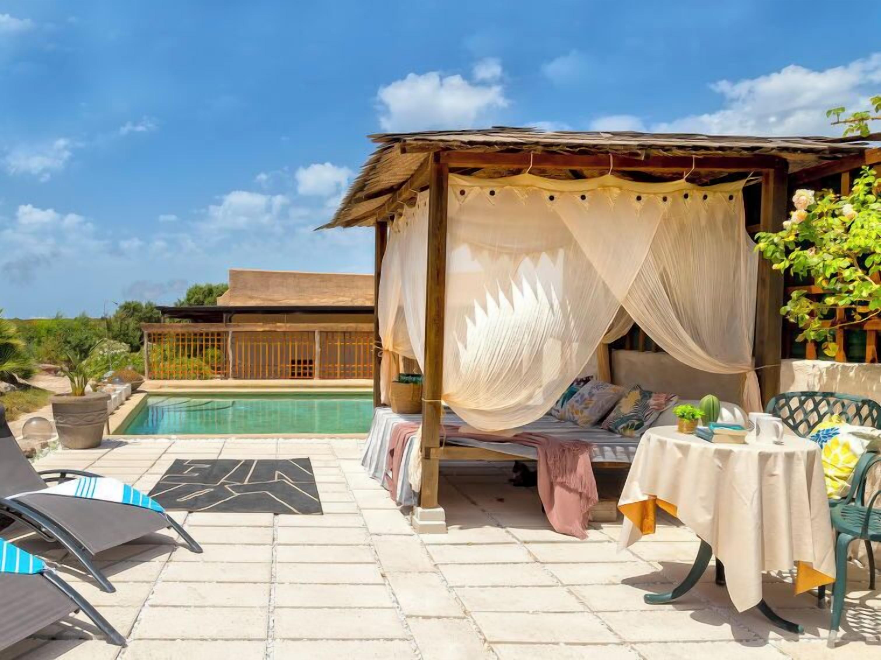 A poolside area with a canopy bed, lounge chairs, and a table with a tablecloth.
