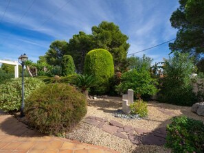 A garden with a variety of plants, a stone bench, and a white pergola.
