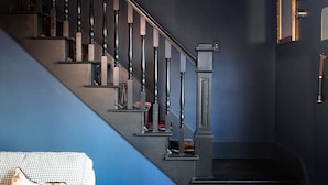 Una sala moderna con un sofá, una mesa de centro, un tapete estampado, una escalera con una pared azul decorativa y un suelo de baldosas blanco y negro.
