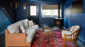 Una sala de estar con pared azul, un sofá, una butaca, una mesa de centro y una chimenea.