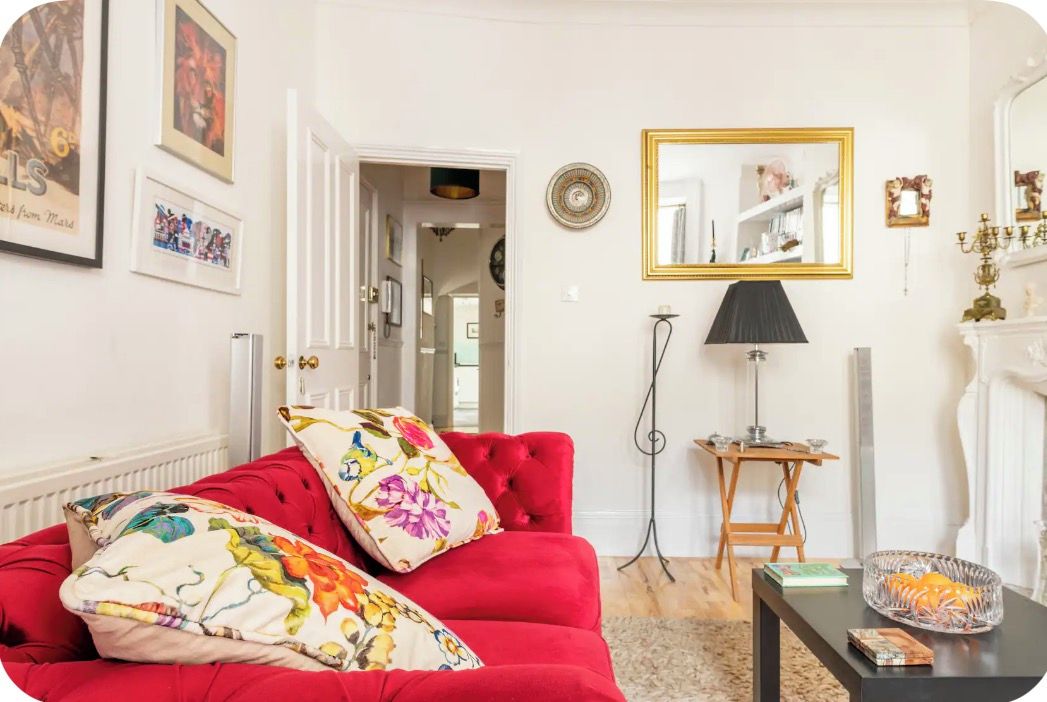 A room with a red sofa, a small table with a lamp, and a mirror on the wall.