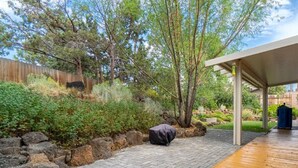 A backyard with a wooden deck, a covered patio, and a stone wall. - Wonderful Updated Single Level Retreat w/ Backyard Oasis, Pet Friendly, A/C, Hot Tub, Private Patio (Bend)